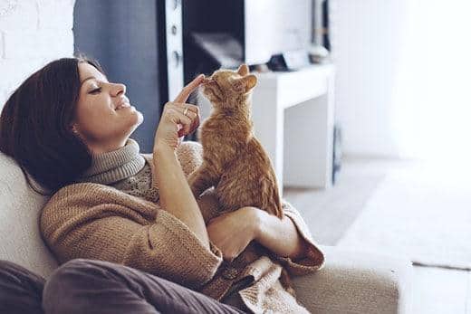 Vrouw die op een stoel zit en een rossige cyperse kat vasthoudt waarbij ze zachtje haar neusje aanraakt 